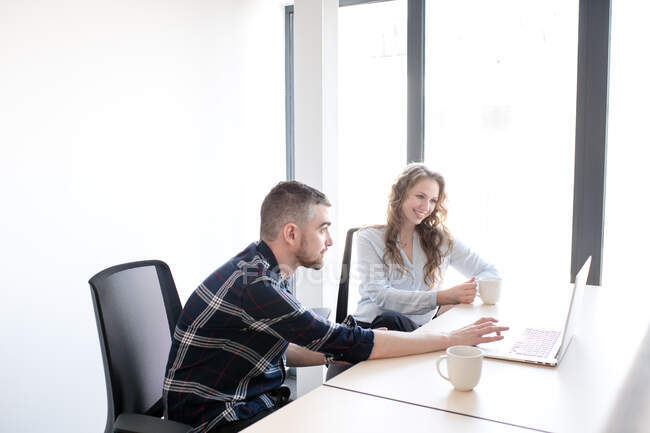 Sorrindo mulher e homem na mesa de escritório assistindo laptop juntos e trabalhando em equipe dentro do escritório moderno — Fotografia de Stock