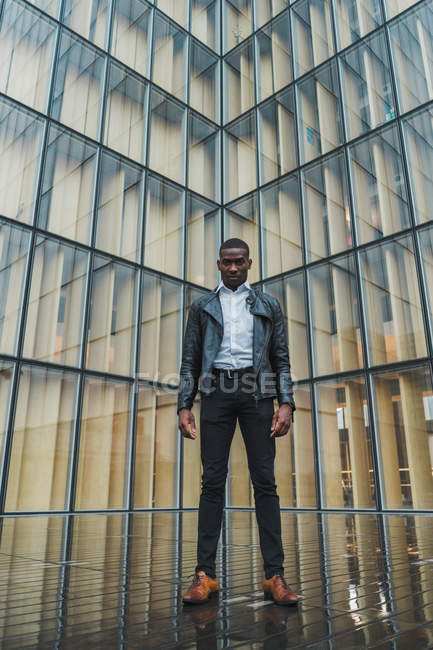 Businessman standing on pavement against modern glass building — Stock Photo