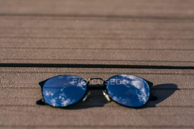 Primo piano di occhiali da sole eleganti neri con riflesso di cielo azzurro che si trova su legno. — Foto stock