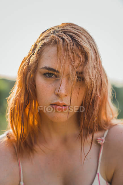 Gros plan d'une jeune femme sérieuse aux cheveux mouillés et aux taches de rousseur regardant la caméra au soleil — Photo de stock