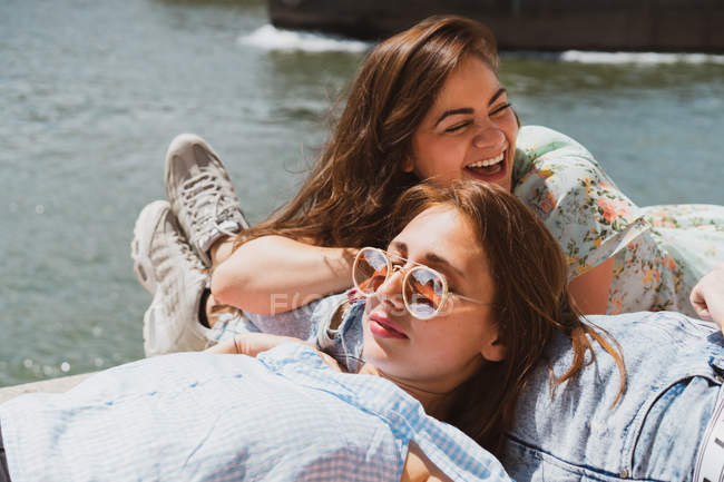 Lächelnde Freundinnen entspannen sich im Sommer am Wasser — Stockfoto