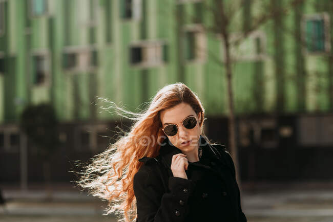Élégante jeune rousse femme en lunettes de soleil regardant la caméra sur fond vert. — Photo de stock