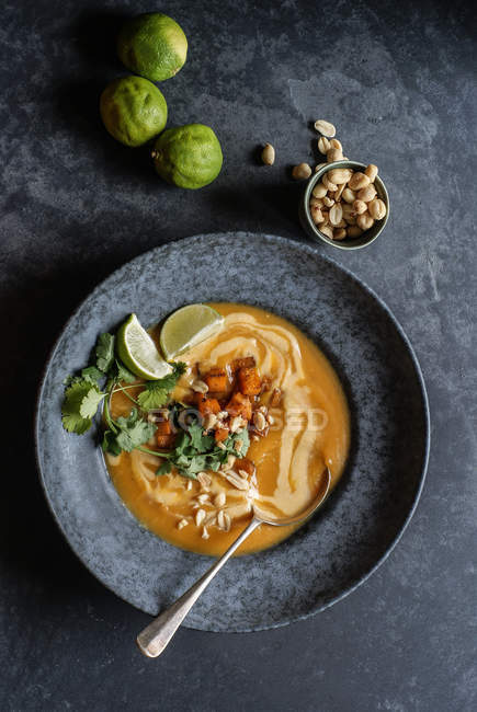 Sopa de abóbora tailandesa com limas e amendoins em placa cinza na superfície cinza — Fotografia de Stock