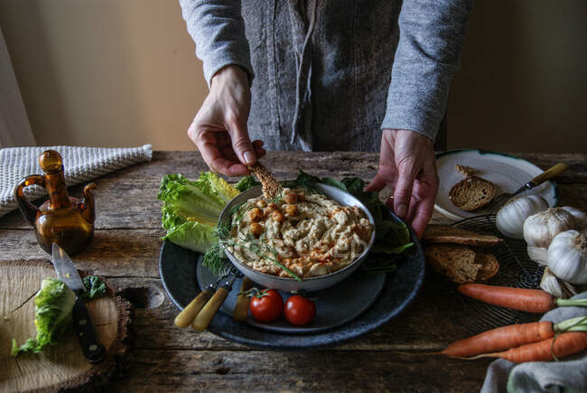 Mani che prendono piatto con delizioso hummus di carciofo — Foto stock