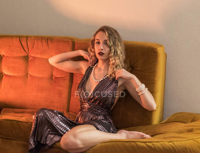 Elegante giovane donna in abito da sera seduta su comodo divano e guardando la fotocamera — Foto stock