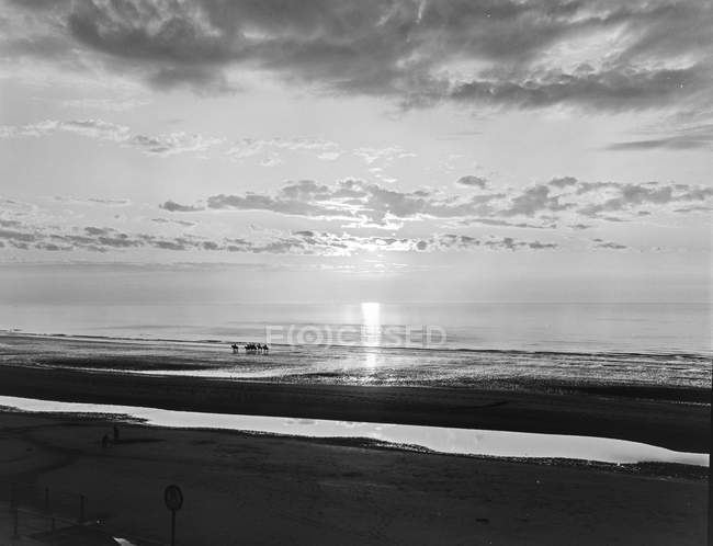 Дрібна вода, що тече на текстурованому піщаному пляжі та хмарному небі — стокове фото