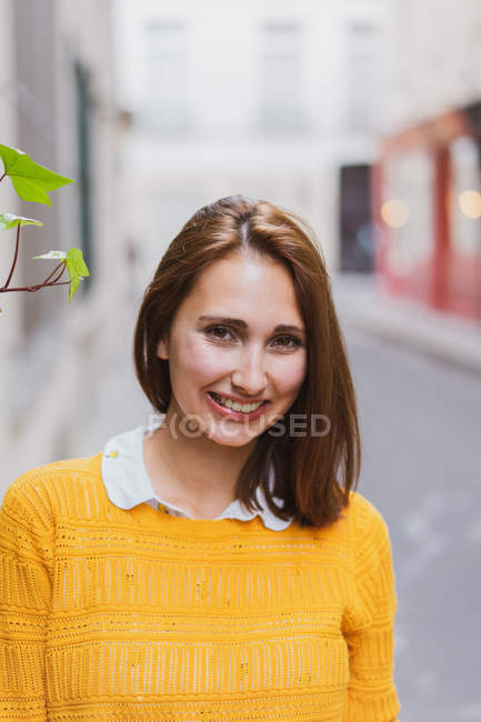 Lächelnde Frau in gelber Strickjacke steht auf der Straße und blickt in die Kamera — Stockfoto