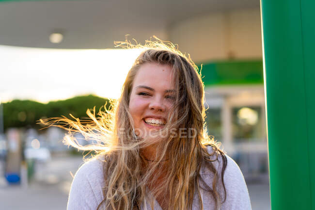 Щаслива молода жінка в повсякденному вбранні дивиться на камеру і сміється в спині, освітленій світлом заходу сонця — стокове фото