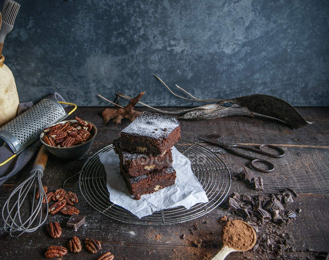 Pezzi di delizioso brownie cioccolato o n rack filo con ingredienti su superficie di legno scuro — Foto stock