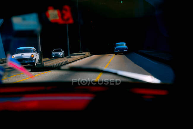 Fotografía tomada desde el interior del coche que muestra la carretera con coches retro que conducen en la ciudad, Cuba - foto de stock