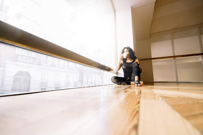 Жінка має каву, сидячи на підлозі в танцювальному класі — стокове фото