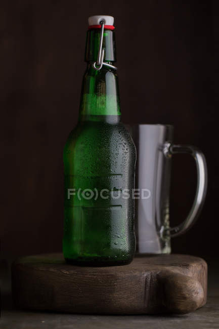 Beer bottle and glass on wooden board on dark background — Stock Photo