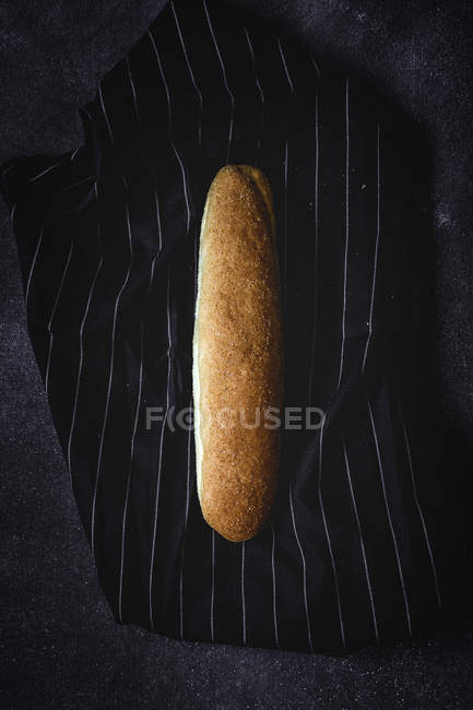 Frisch gebackener Brotlaib auf gestreiftem dunklem Stoff — Stockfoto