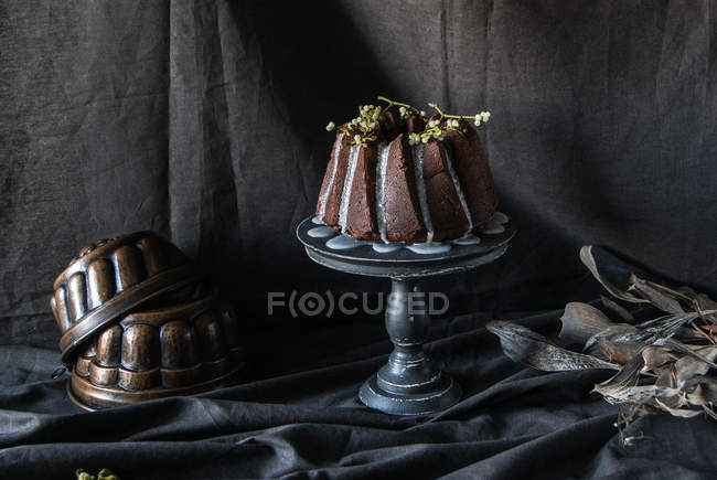 Pastel de chocolate vegano paquete decorado con ramitas de plantas en pie de la torta en tela negra - foto de stock