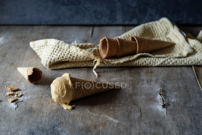 Sorvete saboroso em cone de açúcar crocante com cones vazios na mesa de madeira cinza — Fotografia de Stock