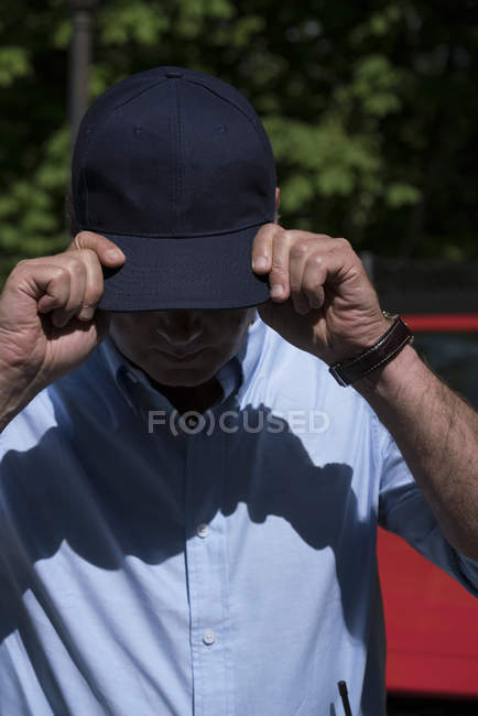 Мужчина в синей рубашке в шапке, стоя на улице под солнцем — стоковое фото