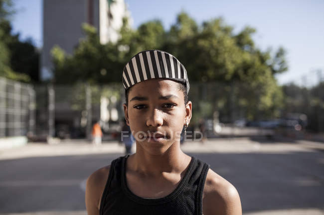 Портрет молодого афро-мальчика в кепке, стоящего на улице и смотрящего в камеру — стоковое фото