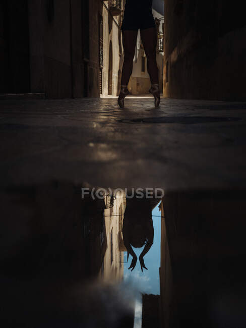 Crop unrecognizable ballet dancer standing on toes and reflecting in the puddle on street. — Stock Photo