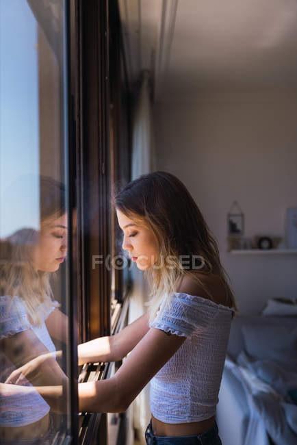 Jovem pensativa olhando pela janela em casa — Fotografia de Stock