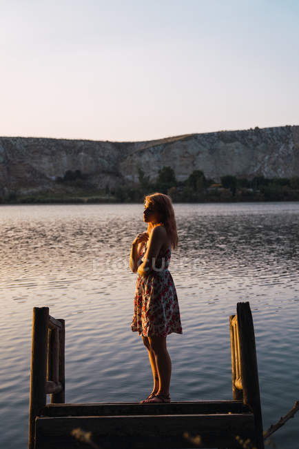 Femme en robe d'été debout sur une jetée coulée au soleil — Photo de stock