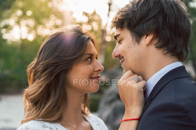 Homem adulto feliz com bela noiva olhando um para o outro em pé na luz do sol ao ar livre e acariciando — Fotografia de Stock