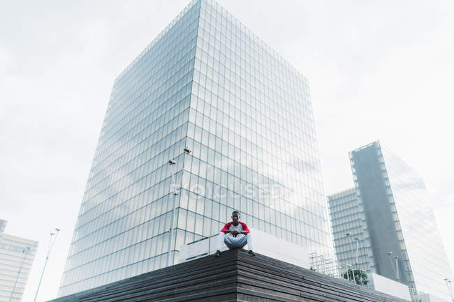 Man in sportswear sitting on stairs with modern glass skyscrapers on background — Stock Photo
