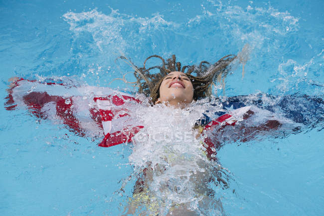 Femme souriante détendue éclaboussant dans la piscine avec drapeau américain — Photo de stock