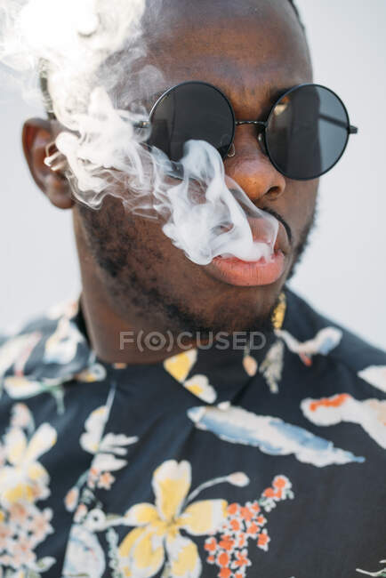 Negro elegante hombre con gafas de sol. Él está vapeando con un cigarrillo electrónico al aire libre - foto de stock