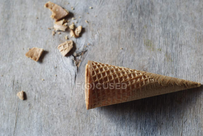 Пустой вафельный рожок для мороженого с крошками на сером деревянном столе — стоковое фото