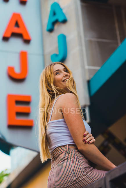 Smiling young woman leaning on fence against building — Stock Photo