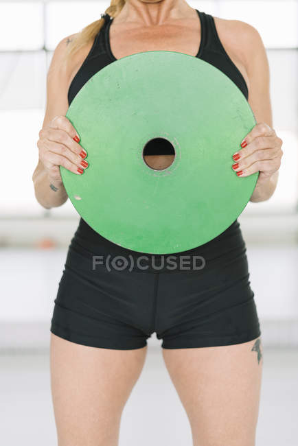Female athlete in black sportswear holding heavy disc and doing exercises while training in gym — Stock Photo
