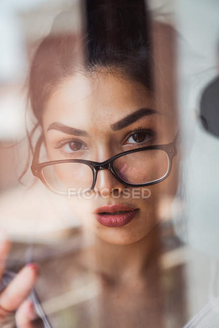 Чуттєва жінка в окулярах дивиться на камеру за вікном — стокове фото