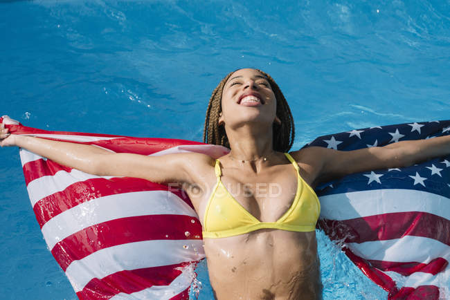 Happy woman having fun in pool with American flag — Stock Photo