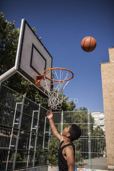 Adolescent garçon visant basket dans panier sur court en plein air — Photo de stock
