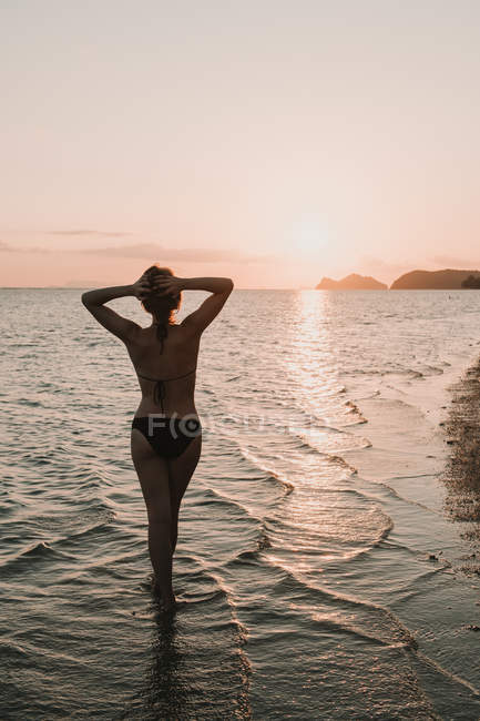 Femme en maillot de bain debout dans l'océan dans les lumières du coucher du soleil — Photo de stock