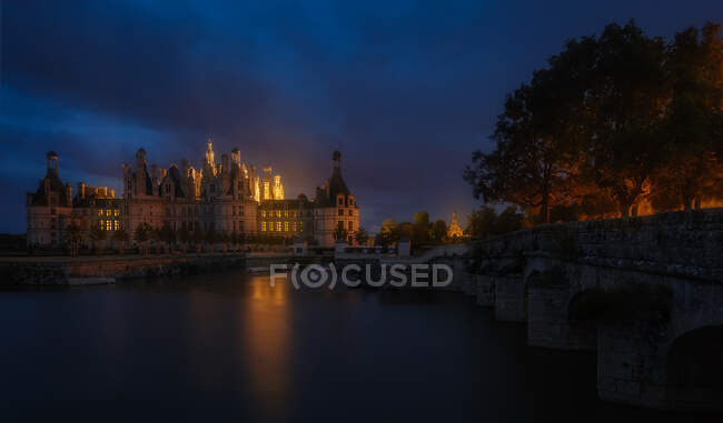 Ponte e incrível castelo medieval em pé na margem do rio à noite em Loire, França. — Fotografia de Stock