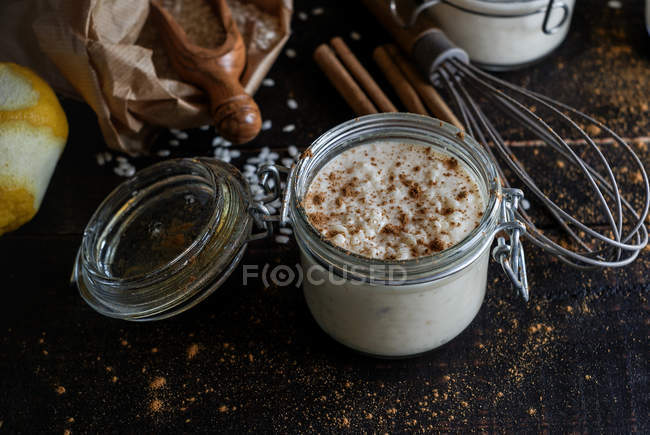 Glass jars of sweet dessert of rice with milk and cinnamon on wooden table with ingredients — Stock Photo