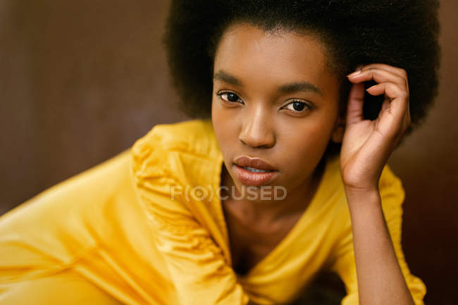 African-American woman in bright yellow dress looking at camera on brown background — Stock Photo