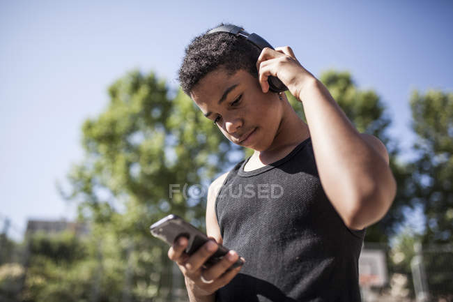 Afro young boy listening to music with smartphone and headphones on basketball court — Stock Photo