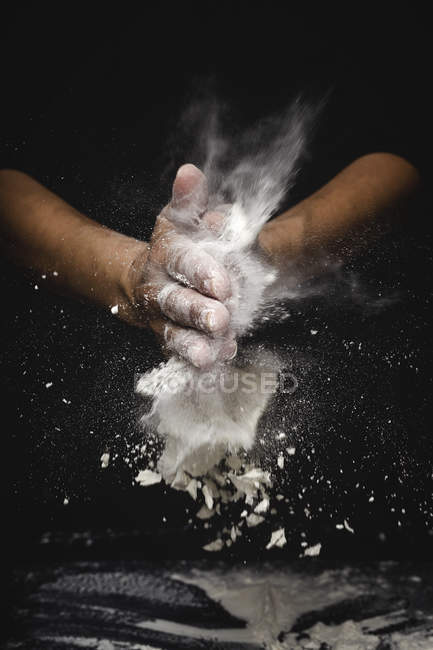 Mains humaines secouant farine et morceaux de pâte sur fond noir — Photo de stock