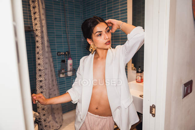 Оголена брюнетка в білій елегантній куртці, що стоїть у ванній — стокове фото