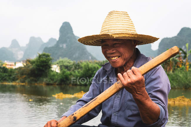 Uomo cinese seduto su zattera sul fiume con le montagne sullo sfondo — Foto stock