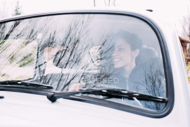 Усміхнена молода жінка водить стару машину і дивиться геть — стокове фото
