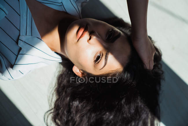 Junge nachdenkliche brünette Frau mit langen Haaren auf dem Boden liegend in Schatten und Sonnenlicht — Stockfoto