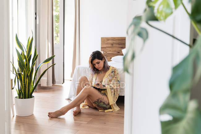 Junge Frau im Seidenmantel sitzt auf dem Boden und zeichnet in Skizzenbuch im stilvollen Schlafzimmer — Stockfoto
