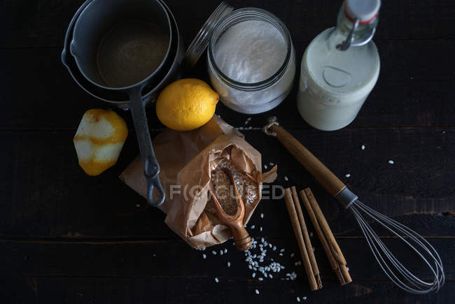 Rustic arrangement of rice, milk, spices and lemons on black wooden table with utensil — Stock Photo