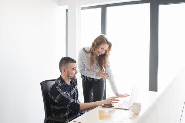 Smiling woman and man at office desk watching laptop together and working in team inside of modern office — Stock Photo