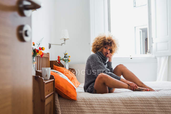Frau im Pullover sitzt auf Bett und blickt in Kamera — Stockfoto
