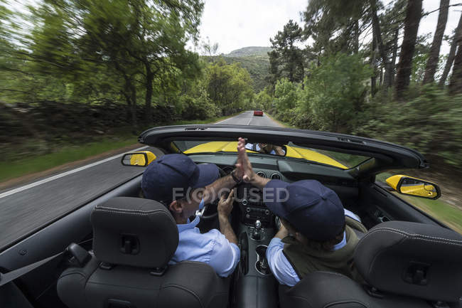 Hommes conduisant dans une voiture rapide moderne en bas de la route dans la campagne — Photo de stock