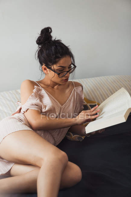 Sensual brunette woman reading book in bed — Stock Photo